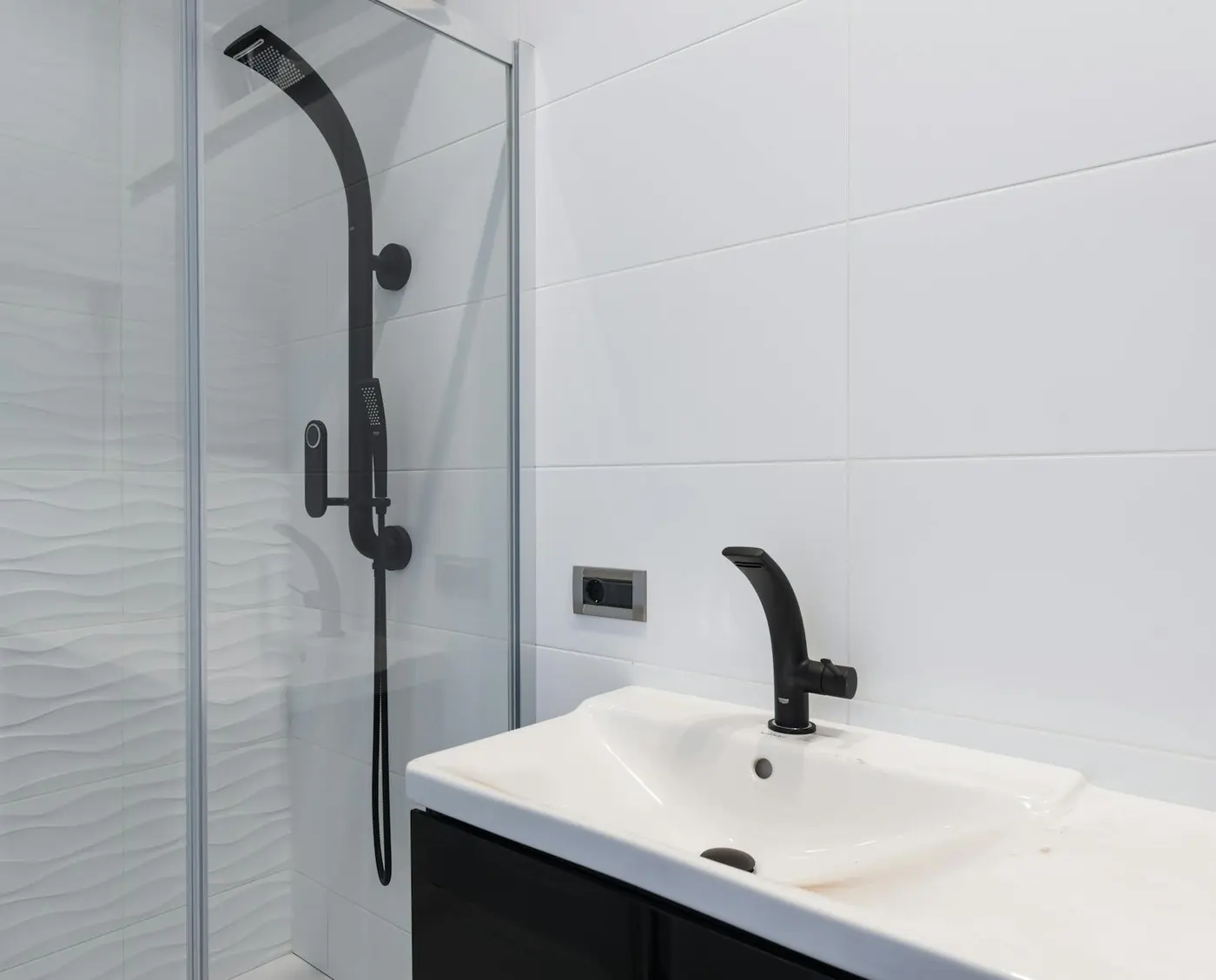 How to Clean Shower Grout Without Damage Moderní koupelna se skleněným sprchovým koutem, bílými obklady a tmavou sprchovou baterií.