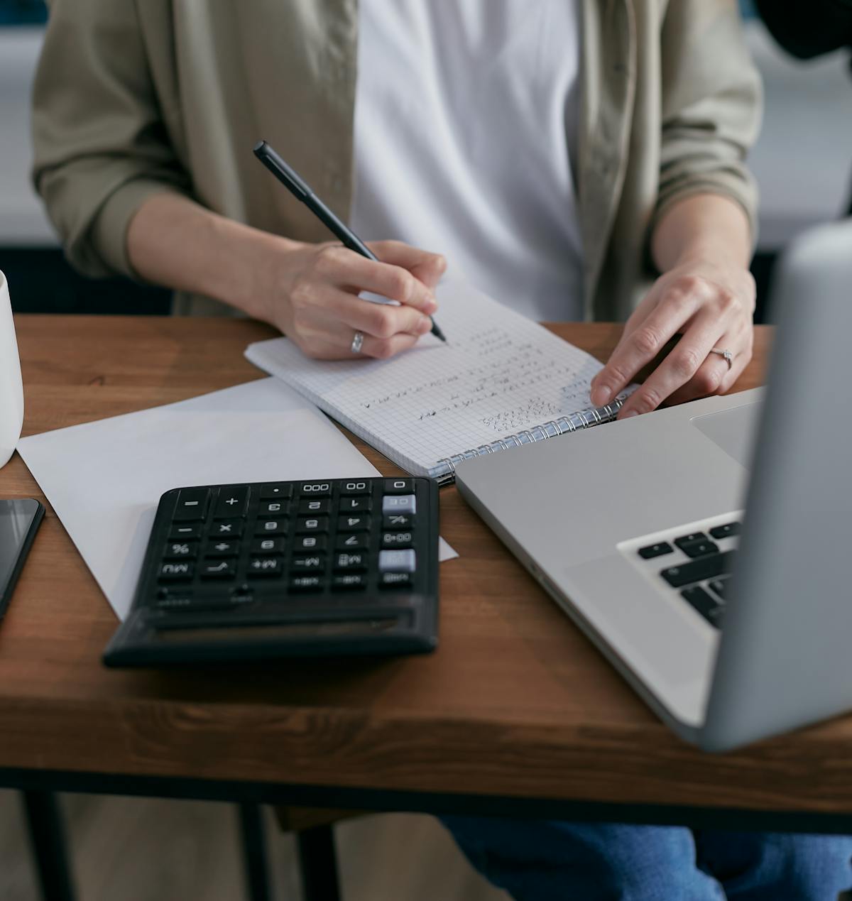 Hands calculating service pricing with a notebook, laptop and calculator on a desk