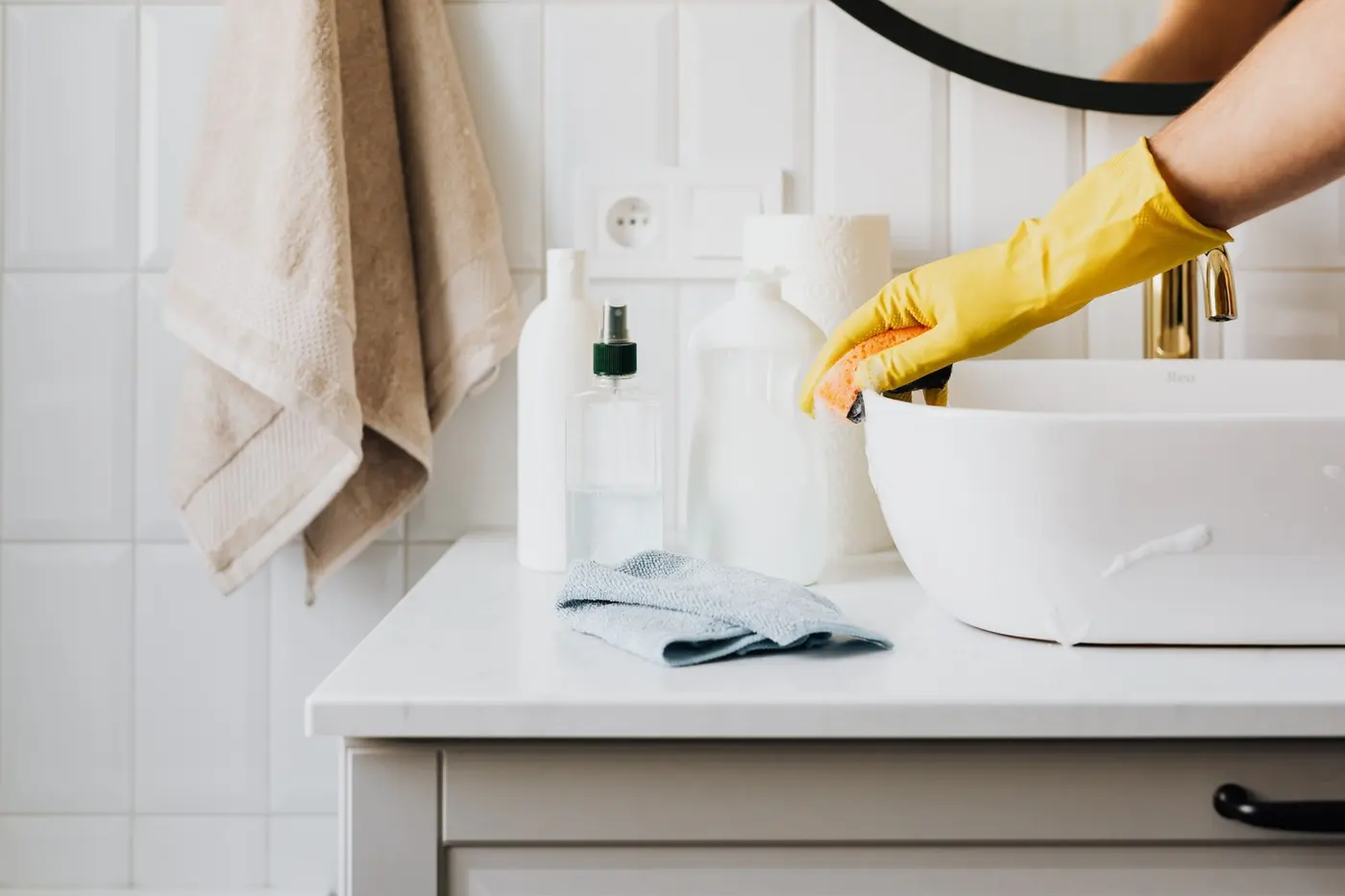 Disinfecting Home After Illness Ruka ve žluté ochranné rukavici utírá houbičkou světlé umyvadlo v moderní domácí koupelně.