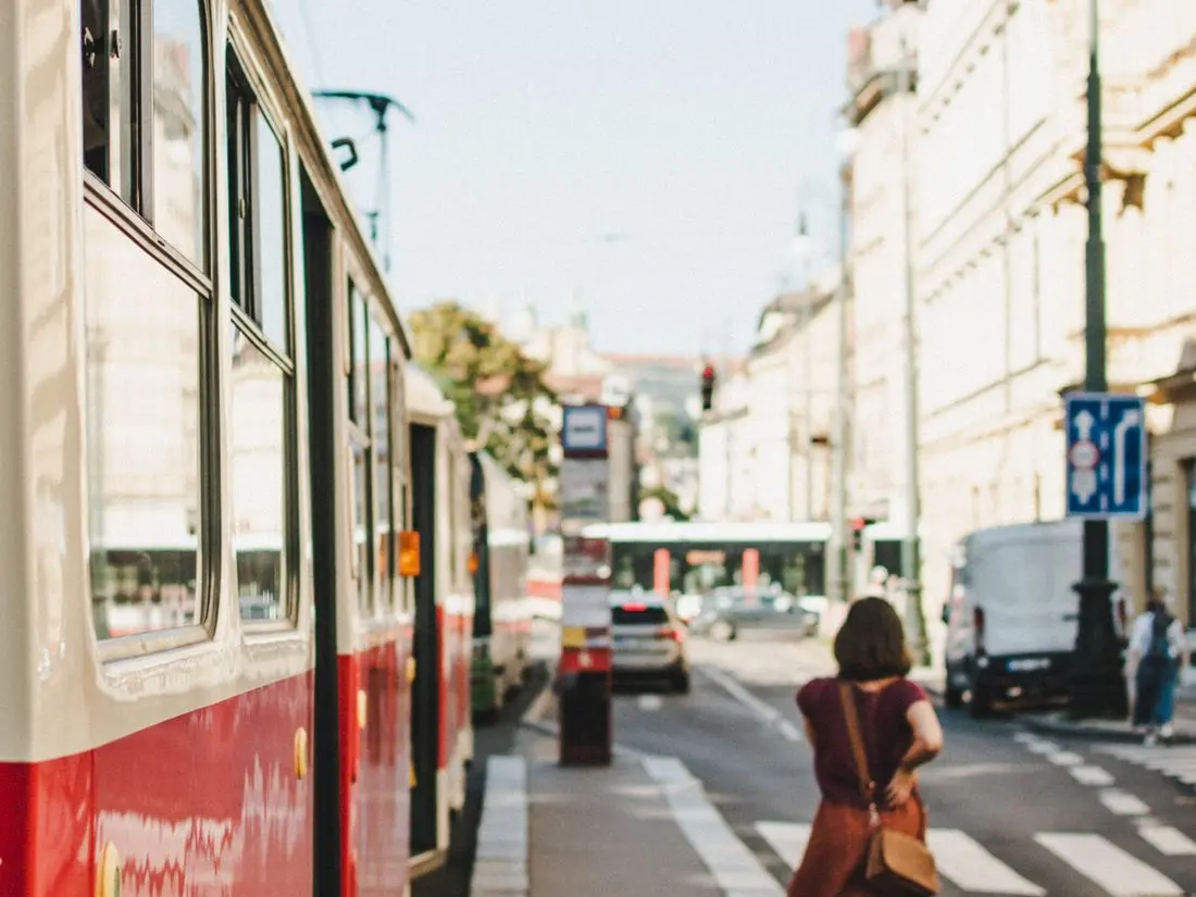 Žena prochází kolem tramvaje na rušné pražské ulici během pracovního dne.