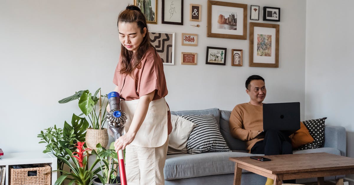 Woman vacuuming the living room while her partner works remotely, showing the time cost of doing your own cleaning