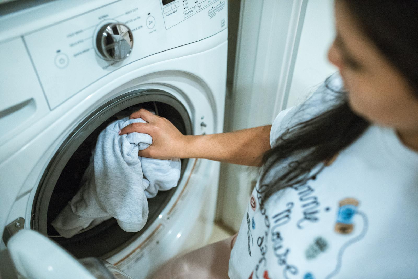 Person loading a front-loading washing machine with the door open
