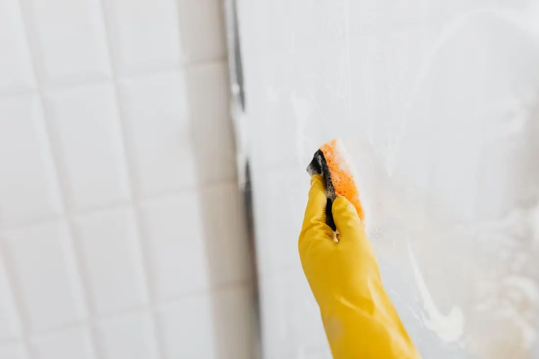 Detail ručního čištění nánosů na skleněné sprchové zástěně