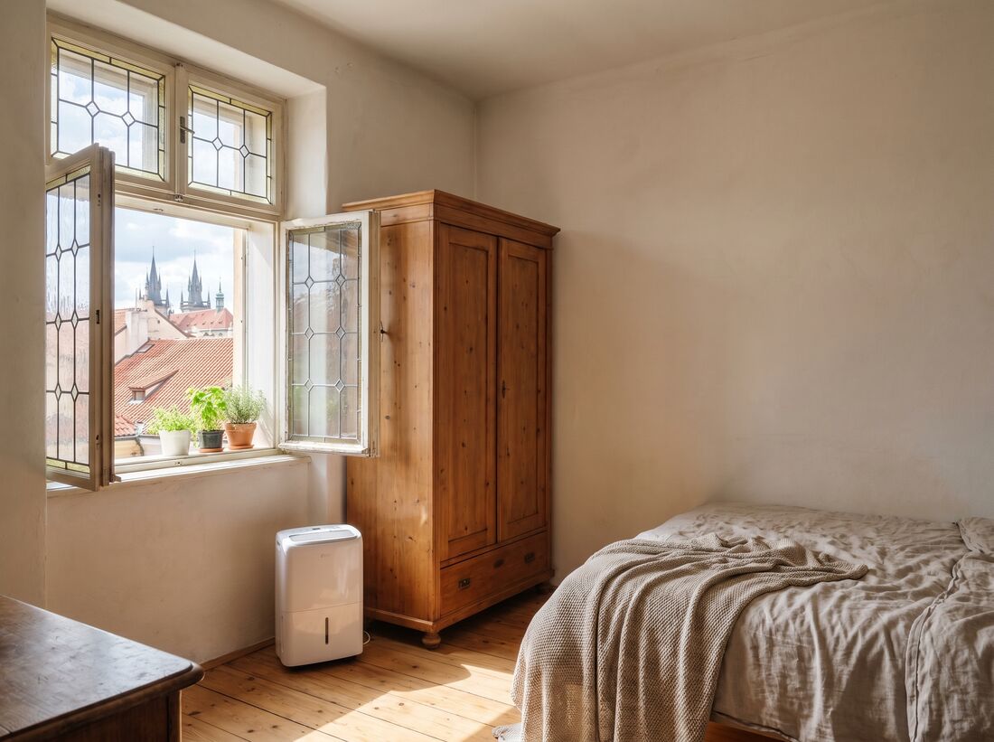 A bedroom with an open window and a wardrobe pulled away from the wall shows how ventilation helps prevent mold.