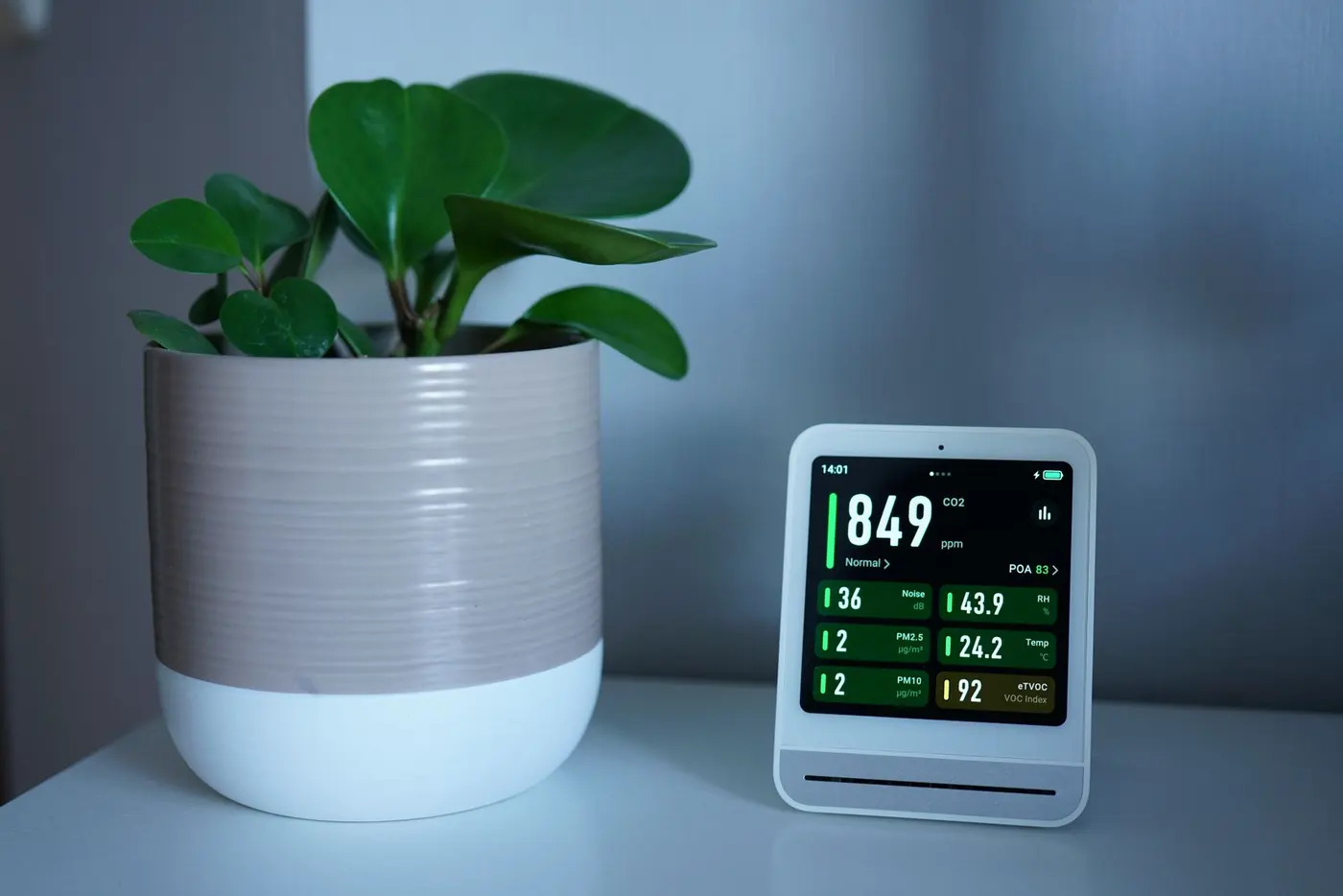 Monitor kvality vzduchu vedle pokojové rostliny ukazuje hodnoty CO₂ a jemných částic