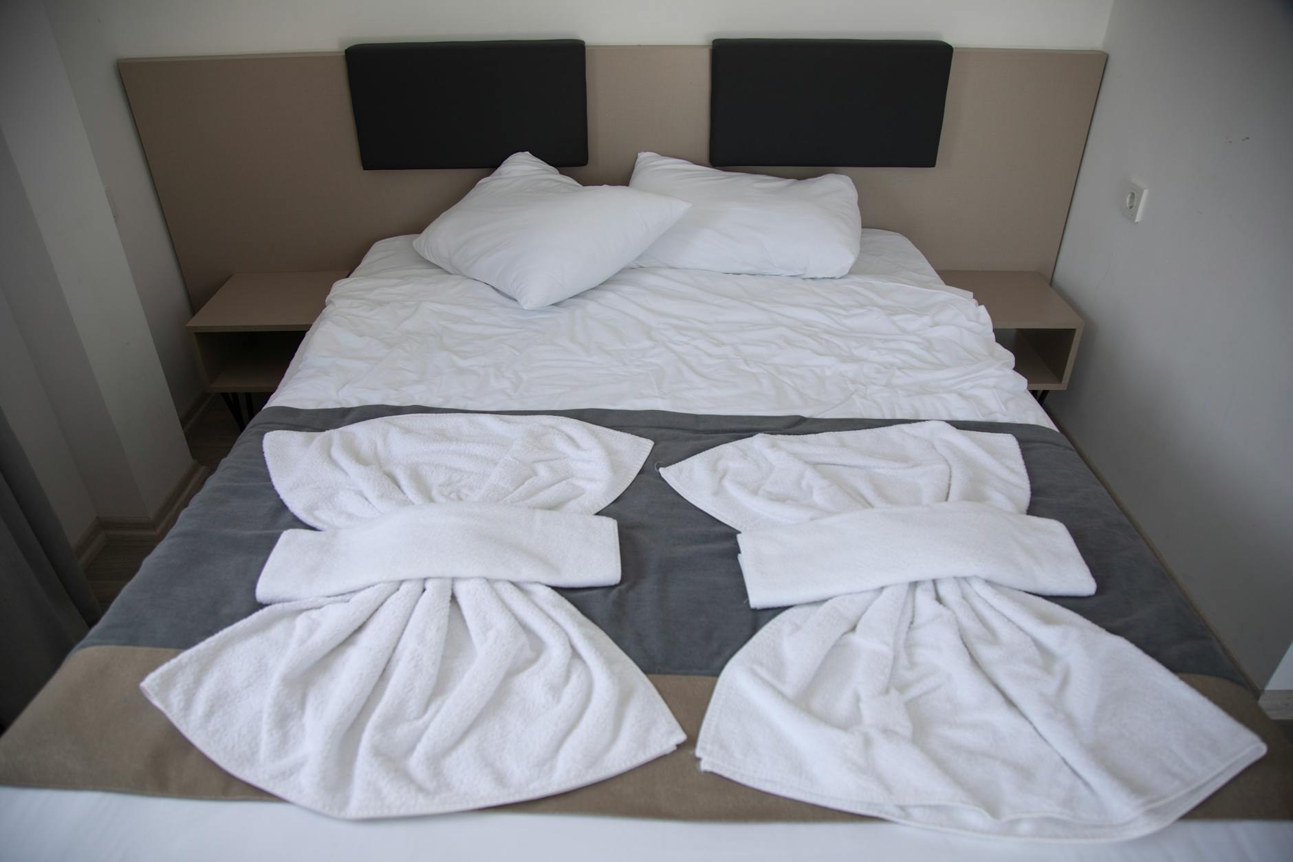 A neatly made guest bed with folded towels and a final pre-arrival apartment check in progress.