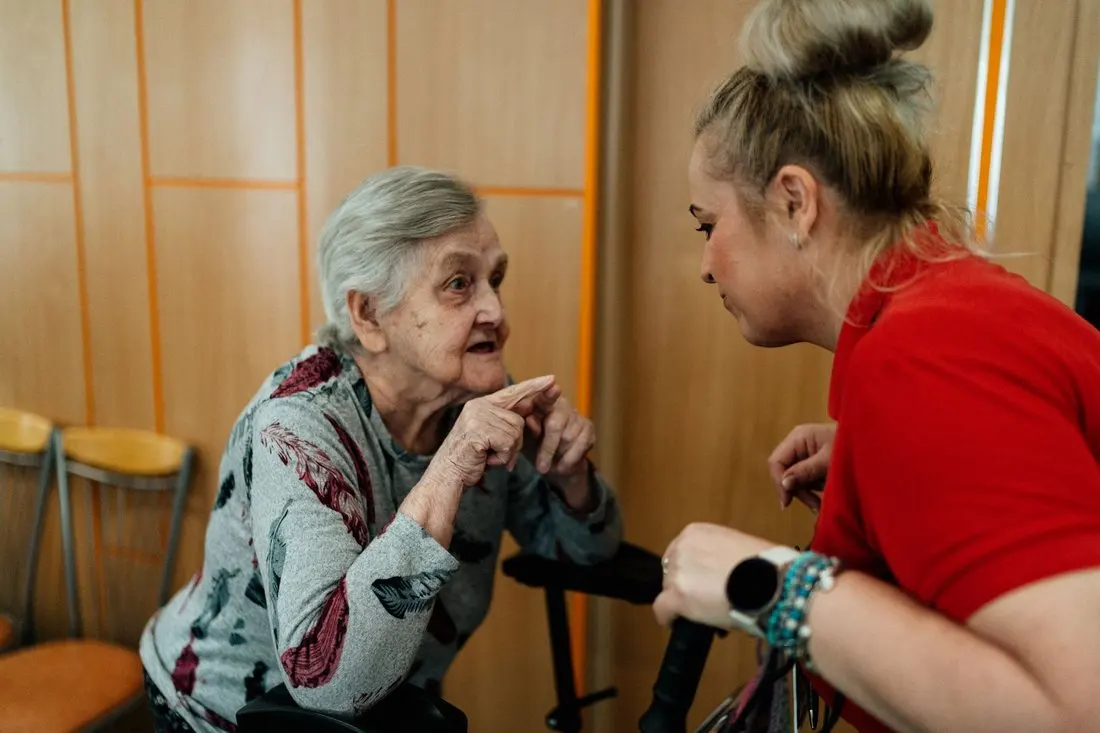 Starší žena doma v klidu hovoří se známou pracovnicí pravidelné služby.