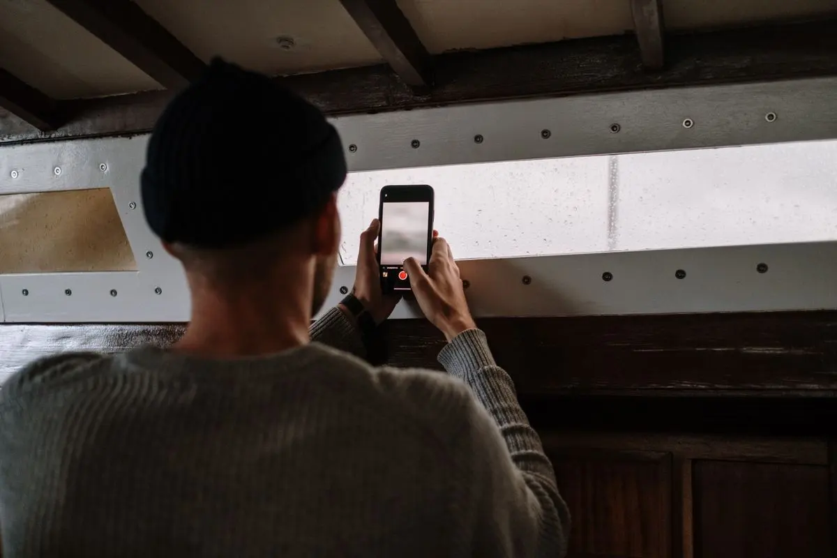 Muž fotografuje pokoj telefonem před domluvou úklidové služby.