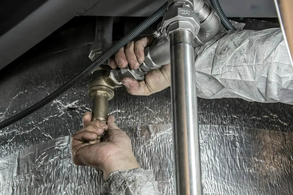Instalatér kontroluje a montuje potrubní spoje při řešení technického problému.
