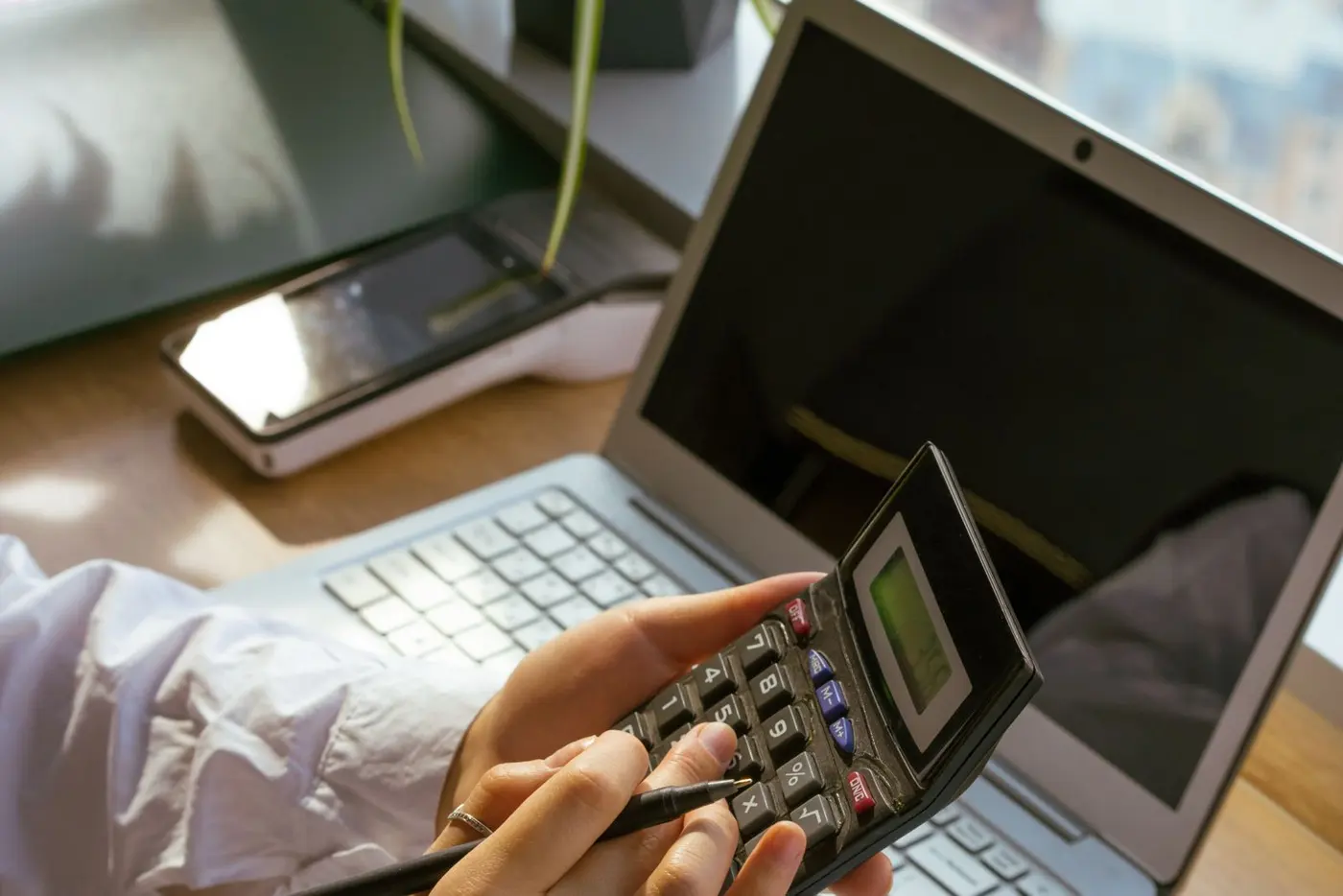 Samostatná podnikatelka u pracovního stolu počítá na kalkulačce a plánuje nové ceny úklidu.